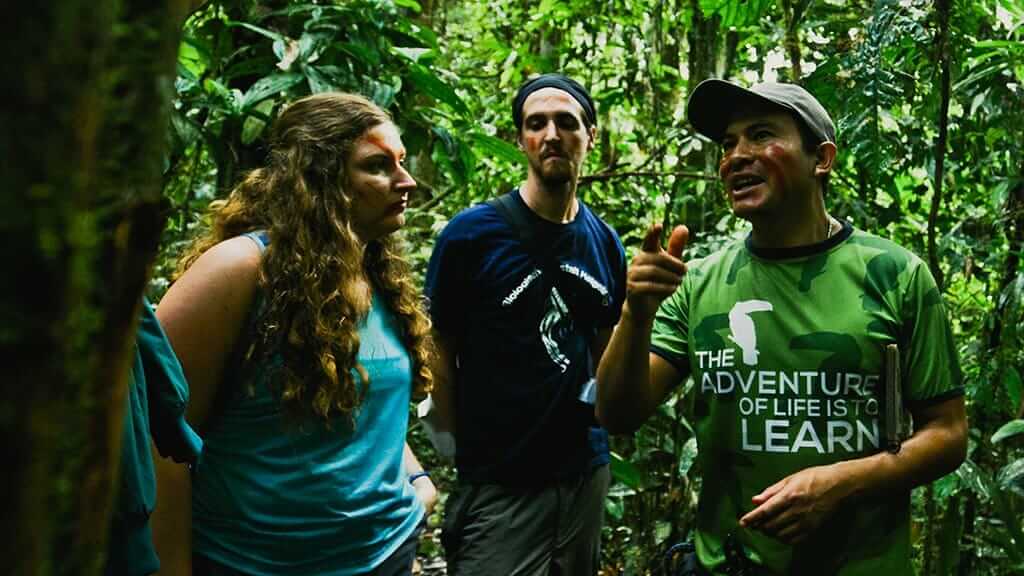 Los turistas escuchan al guía turístico nativo en la selva con caras pintadas.