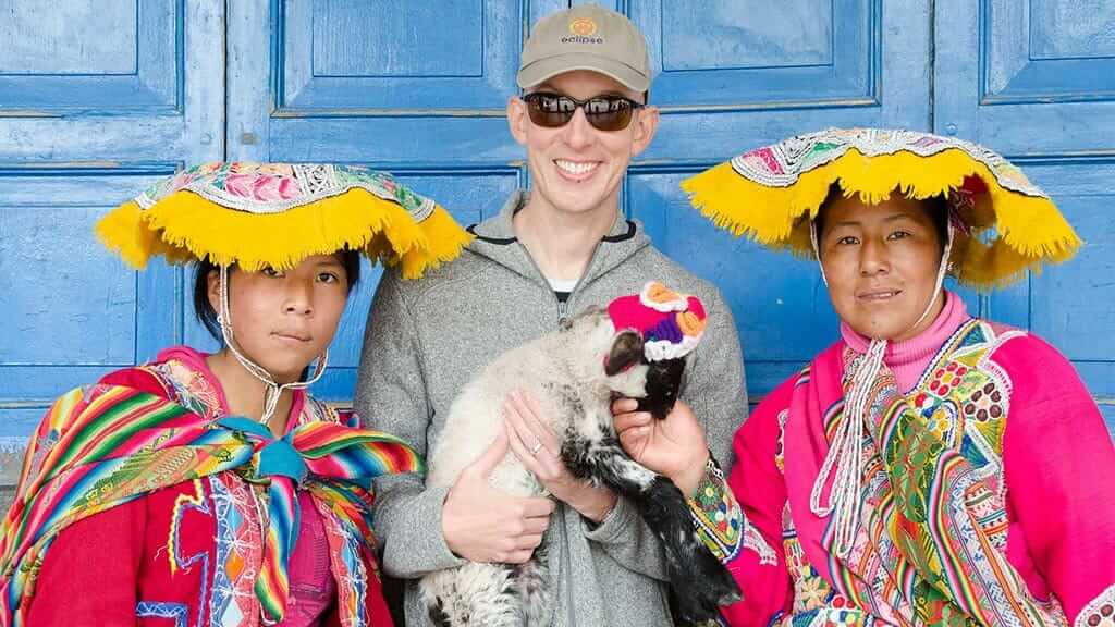 tourist with indigenous ladies and lamb in front of blue colonial door in cusco peru
