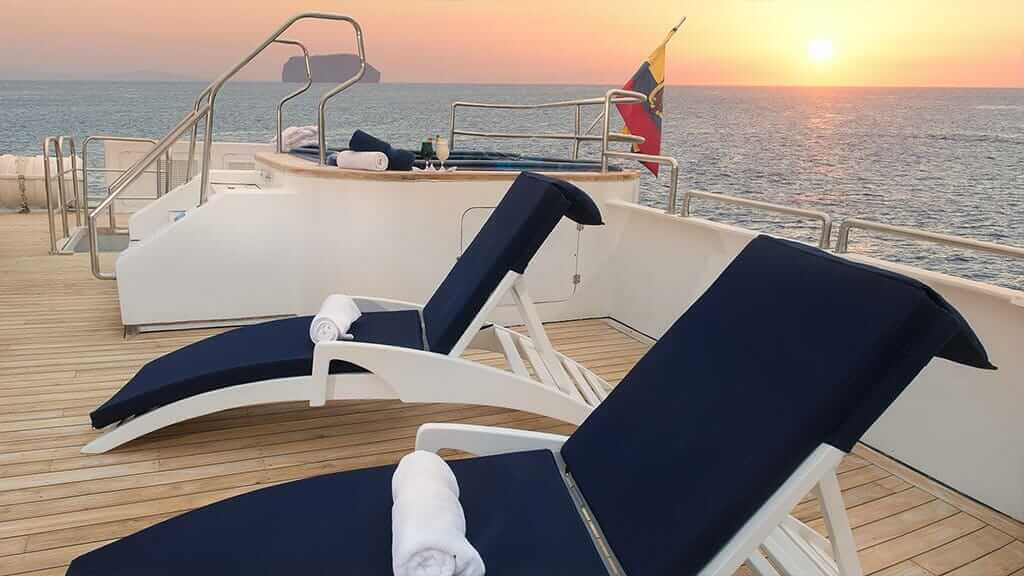 cormorant catamaran yacht galapagos island cruise - sundeck loungers and jacuzzi with setting sun background