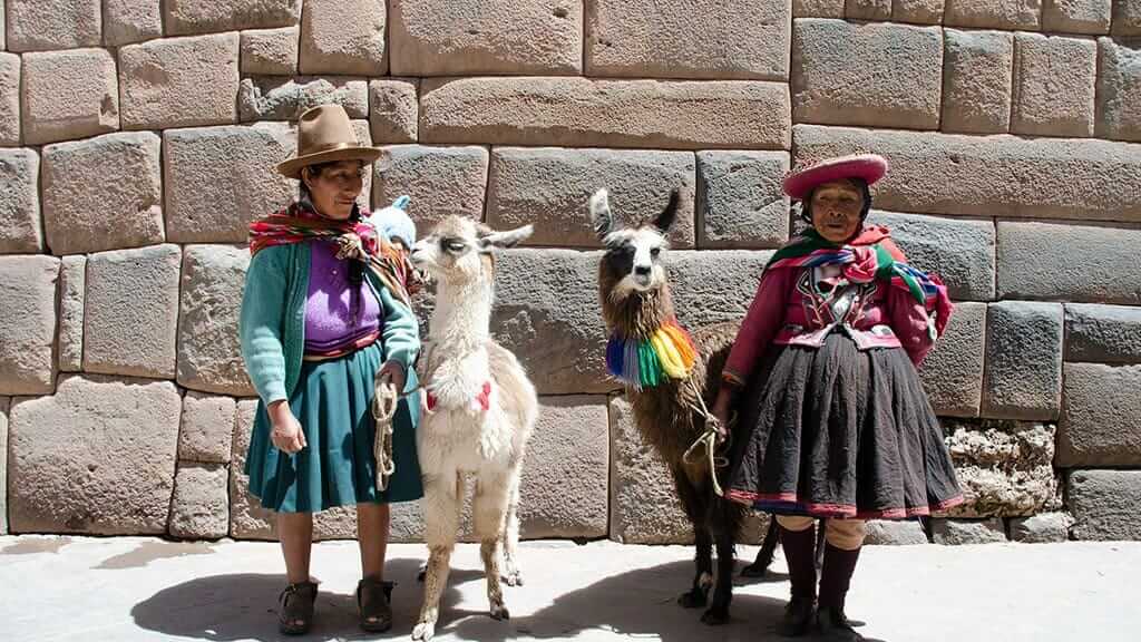 indigenous women with llamas in front of inca wall in cusco peru