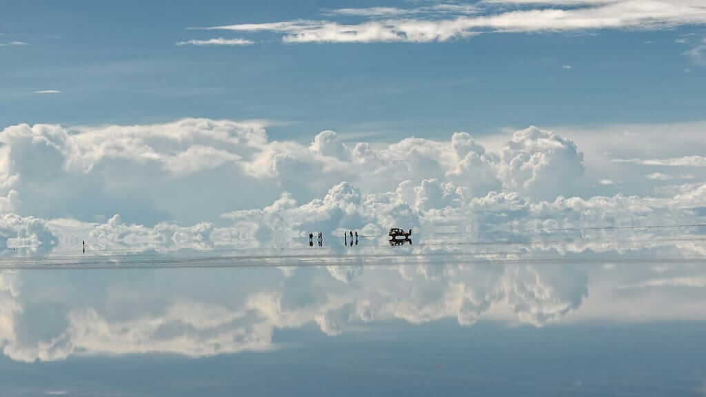 Jeep and tourists on salar de uyuni salt flats with clouds and relflection