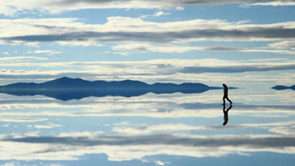 Touristen, die mit bizarrer Reflexion auf durchnässten Salar de Uyuni-Salinen mit Wolken gehen
