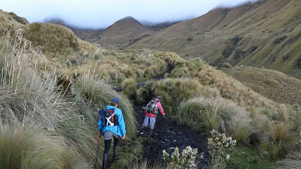 two tourists hike through mud and grass at al altar ecuador