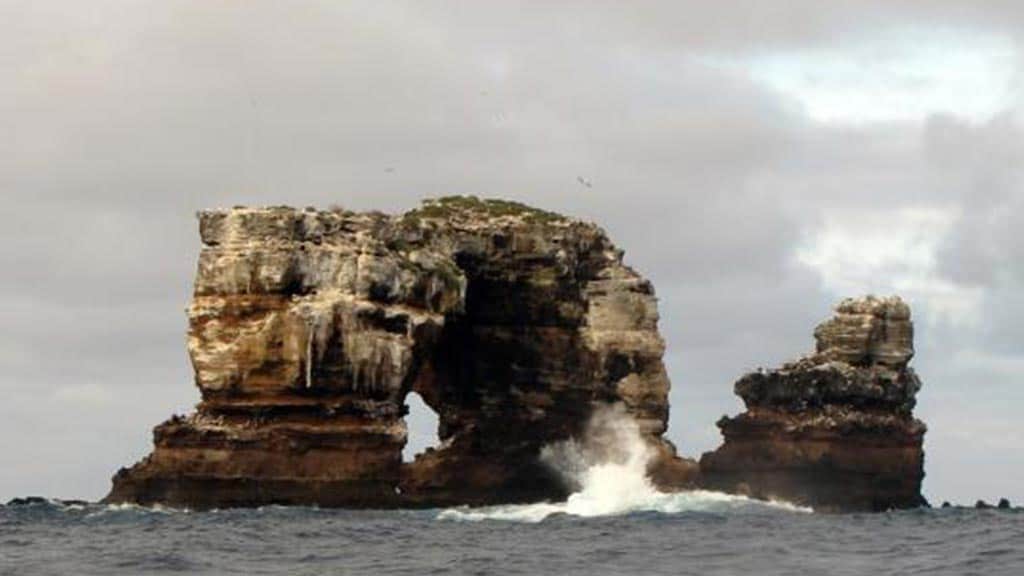 a wave crashes against darwins arch at darwin island galapagos