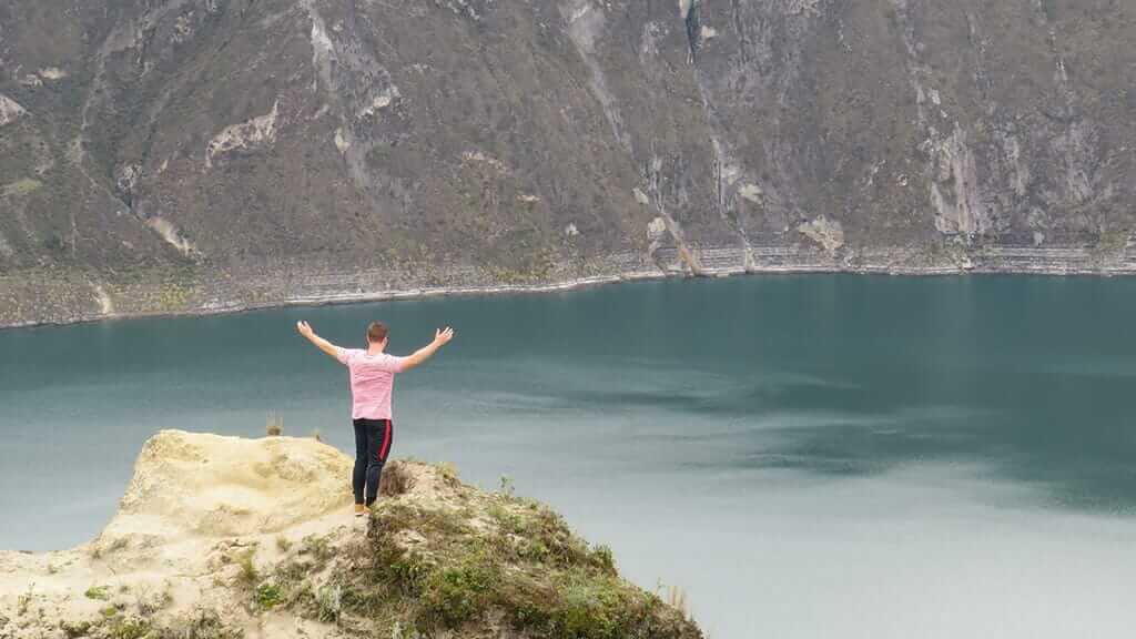 a tourist with outstretched arms with spectacular quilotoa lagoon in the background