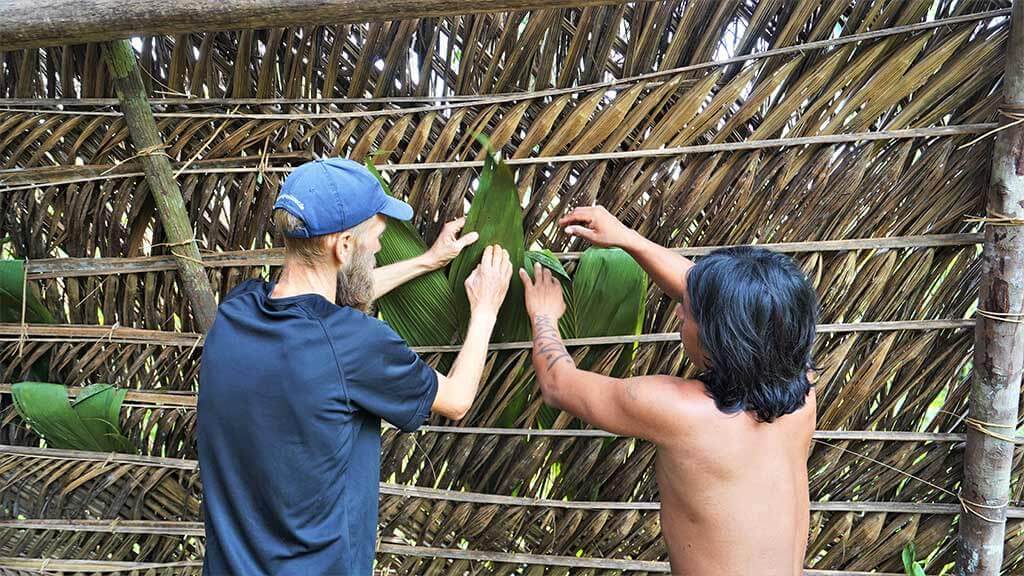 wuaorani indian teachig tourist to thatch roof of jungle hut